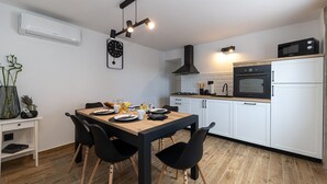 A modern kitchen with white cabinets, a black stove, and a microwave. There is a dining table with chairs and a clock on the wall. - Mediterranean villa with private pool, sea view, dog-friendly, barbecue, private parking (Grižane)