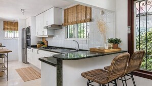 Cuina moderna amb armaris blancs, un refrigerador d'acer inoxidable i una illa gran amb tamborets.