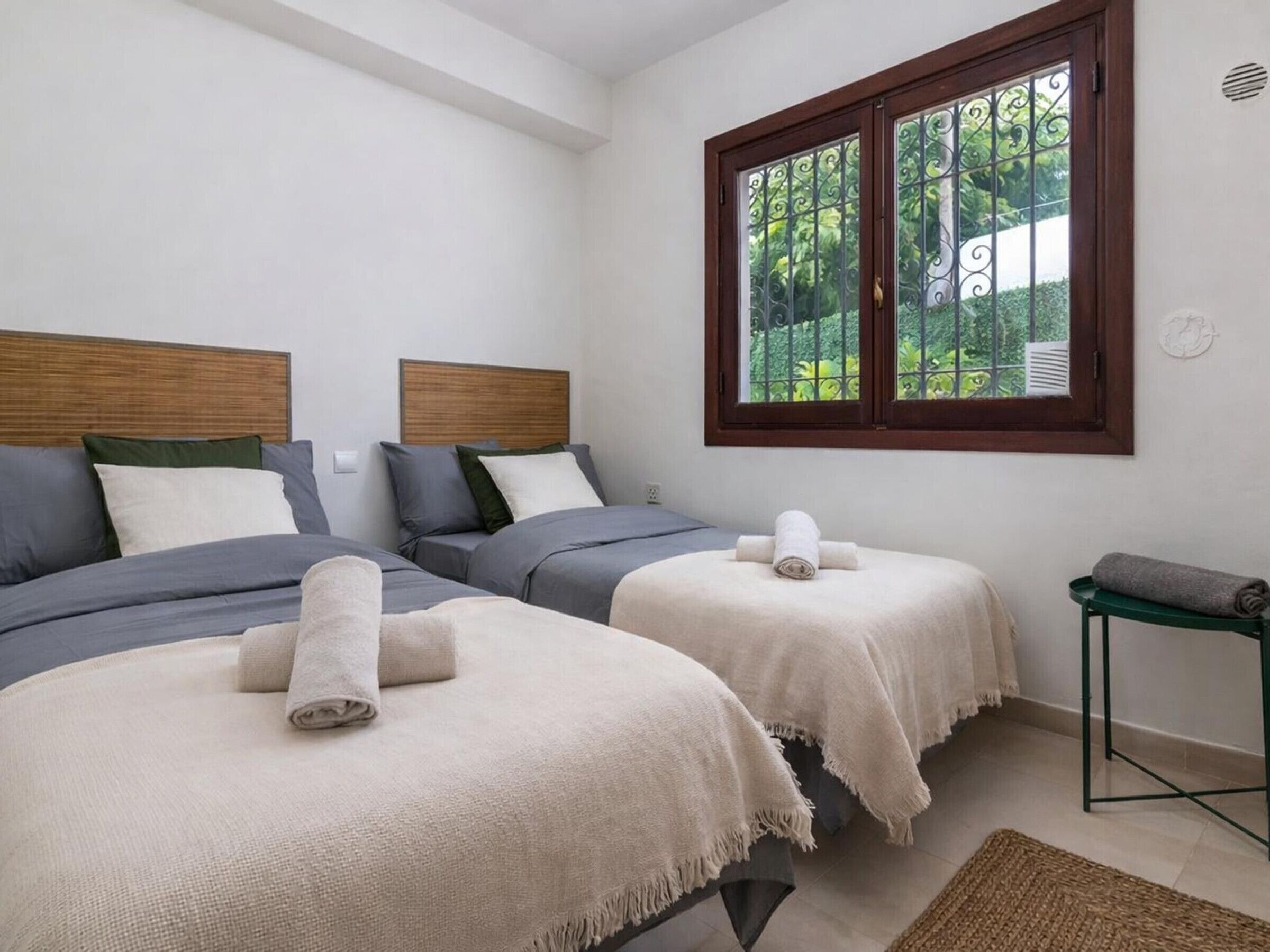 Een slaapkamer met twee bedden, een raam met uitzicht op groen en een klein tafeltje met een handdoek.