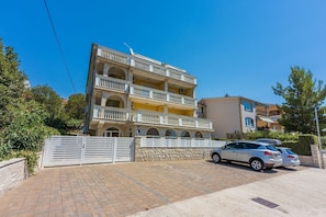 A multi-story residential building with balconies, a gated driveway, and parked cars. - Charming apartment just 800 metres from the beach with stunning sea views (Crikvenica)