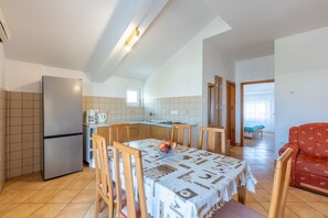 A compact kitchen with a refrigerator, a coffee maker, and a dining table with chairs. There is a red sofa in the living area. - Charming apartment just 800 metres from the beach with stunning sea views (Crikvenica)