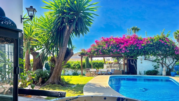 A poolside area with a clear view of the pool, a wooden deck, and a pergola with pink flowers. - Villa Alfredo in Estepona: 4 bedrooms near the beach (Estepona)