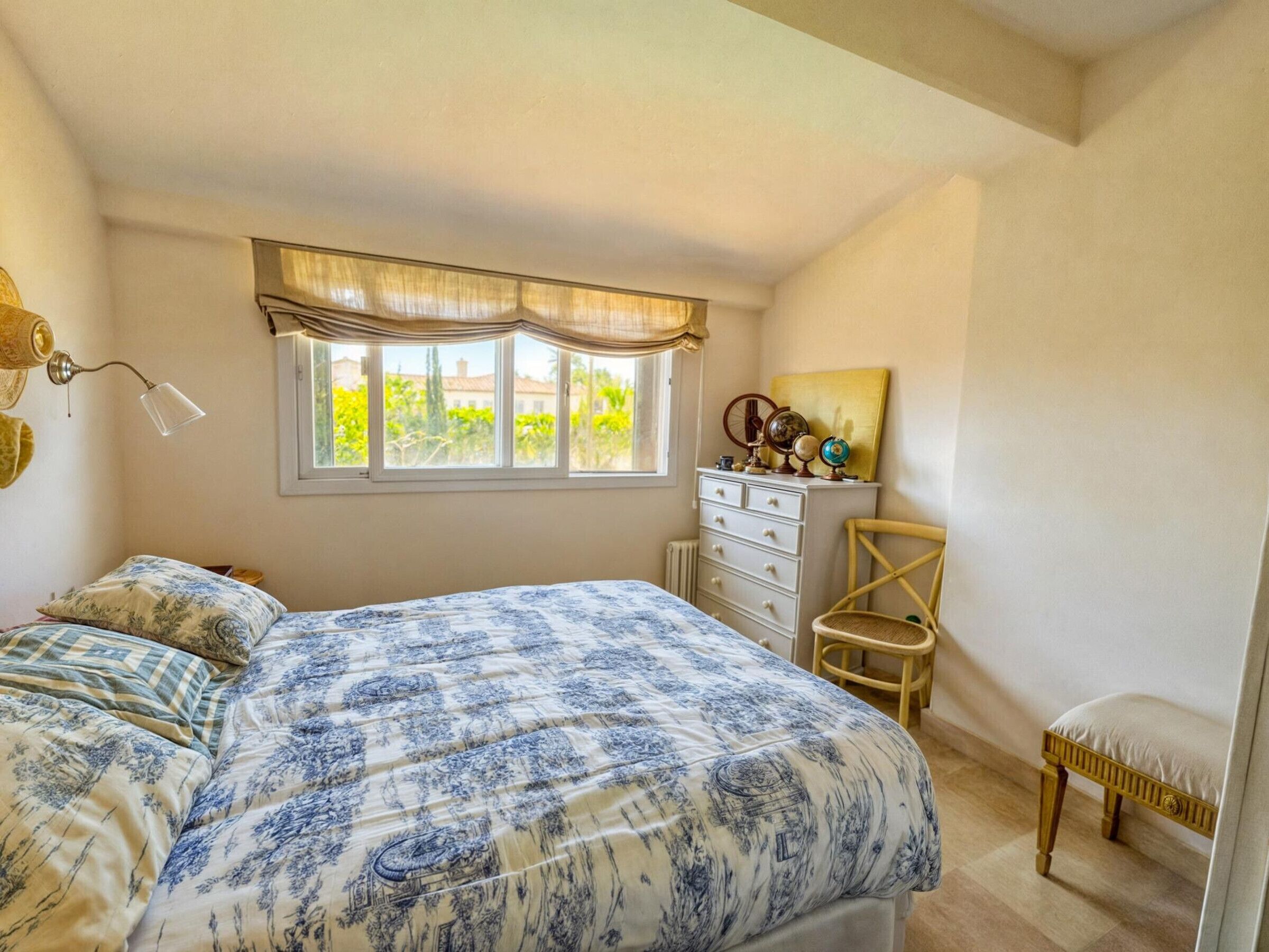 Ein Schlafzimmer mit einem großen Bett, einem Schminktisch, einem Sessel und einem Fenster mit Vorhängen.