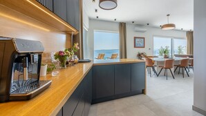 Eine moderne Küche mit integrierter Kaffeemaschine, einer zentralen Kochinsel mit Sitzgelegenheiten und Meerblick durch große Fenster.