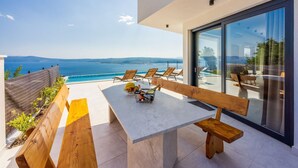 Eine moderne Außenpatio mit Meerblick, ausgestattet mit einem Esstisch, Holzbänken und Loungestühlen.