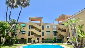 Ein mehrstöckiges Hotel mit Swimmingpool, umgeben von Palmen und Grünpflanzen.