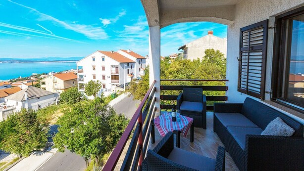 Ein Balkon mit Gartenmöbeln, einem Tisch mit Flasche und Gläsern sowie Blick auf Gebäude und das Meer.