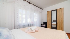 Ein Schlafzimmer mit einem Bett, einem Sessel, einem Kleiderschrank und durchsichtigen Vorhängen.