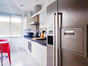 Une cuisine moderne avec des appareils en acier inoxydable, une chaise rouge et une fenêtre avec des stores.