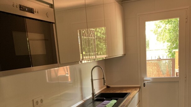 Eine moderne Küche mit weißen Schränken, einer Holzarbeitsplatte, einem eingebauten Backofen und einem Fenster mit Blick auf Grünflächen.