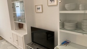 Ein Wohnzimmer mit Flachbildfernseher, Glasvitrinen und gerahmten Bildern an der Wand.