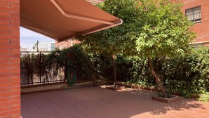 Eine Terrasse mit Pflasterboden, einer Pergola und einem Garten mit verschiedenen Pflanzen und einem Baum.