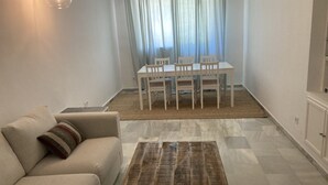 Ein Wohnzimmer mit einer Couch, einem Couchtisch, einem Esstisch mit Stühlen und einem Fenster mit Vorhängen.