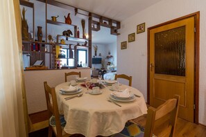 Ein Essbereich mit einem runden Tisch, gedeckt für vier Personen, umgeben von Holzstühlen. Im Hintergrund ist ein dekorativer Schrank mit verschiedenen Gegenständen zu sehen.
