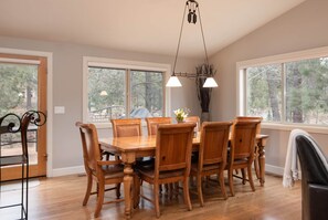 Un espace repas avec une table et des chaises en bois, de grandes fenêtres et un luminaire suspendu.