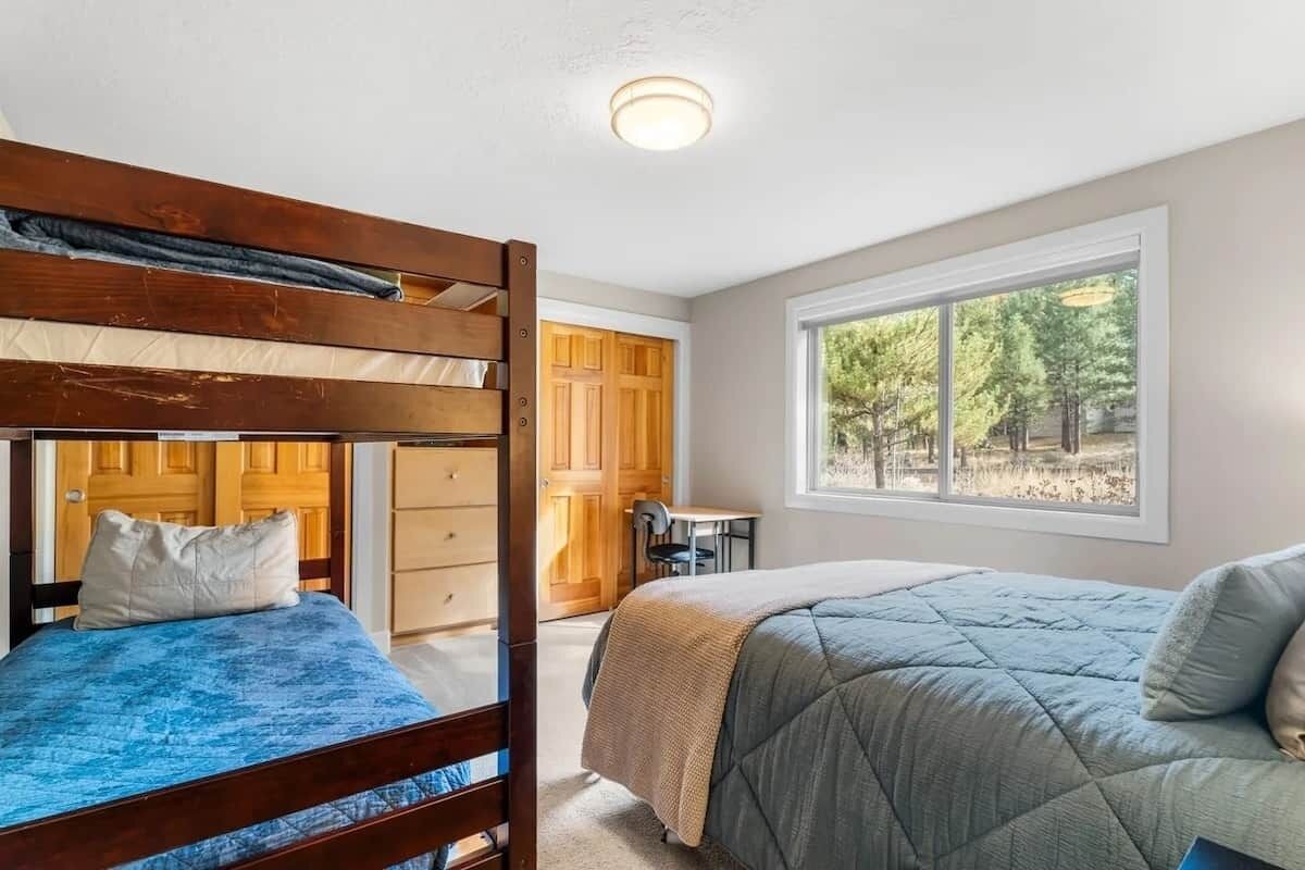 A bedroom with two beds, a window with a forest view, and a door leading to a bathroom.
