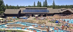 Un complexe hôtelier doté de plusieurs piscines, d’un grand bâtiment équipé de panneaux solaires et entouré d’une forêt.