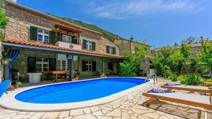 Eine Steinvilla mit Swimmingpool, Sitzgelegenheiten im Freien und Bergblick.
