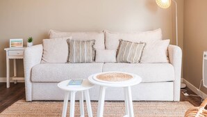 A cozy living room with a light-colored sofa, two white side tables, a floor lamp, and a small plant on a white nightstand. - Comfortable Studio in Le Touquet Near Beach (Le Touquet-Paris-Plage)