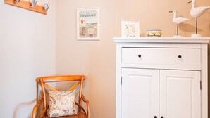 A wooden chair with a patterned cushion, a white cabinet with two doors, and a wall-mounted shelf with a framed picture and decorative items. - Comfortable Studio in Le Touquet Near Beach (Le Touquet-Paris-Plage)