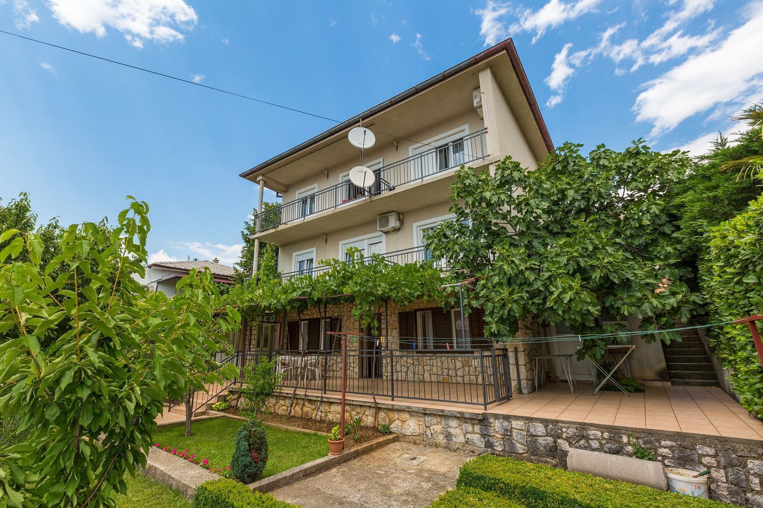 A two-story building with a balcony, surrounded by lush greenery and a stone pathway.