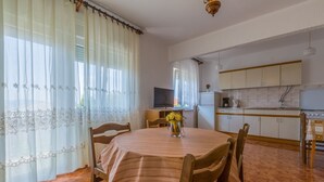 Een eetgedeelte met een ronde tafel, stoelen, een televisie en een keuken op de achtergrond.