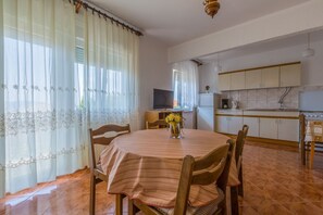 A dining area with a round table, chairs, a TV, and a kitchen in the background. - Charming apartment just 650 metres from the beach with sea views, BBQ area, private parking (Novi Vinodolski)