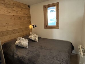 A bedroom with a wooden headboard, two pillows, a window with a view, and a radiator. - Renovated studio cabin in Les Saisies for 4 people, terrace (Les Saisies)