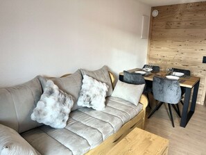 A modern living room with a sofa, a coffee table, and a dining area with chairs and a table. - Renovated studio cabin in Les Saisies for 4 people, terrace (Les Saisies)