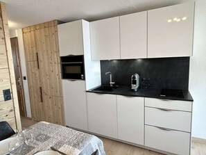 A modern kitchen with white cabinets, a black countertop, a built-in microwave, a sink, and a stove. - Renovated studio cabin in Les Saisies for 4 people, terrace (Les Saisies)