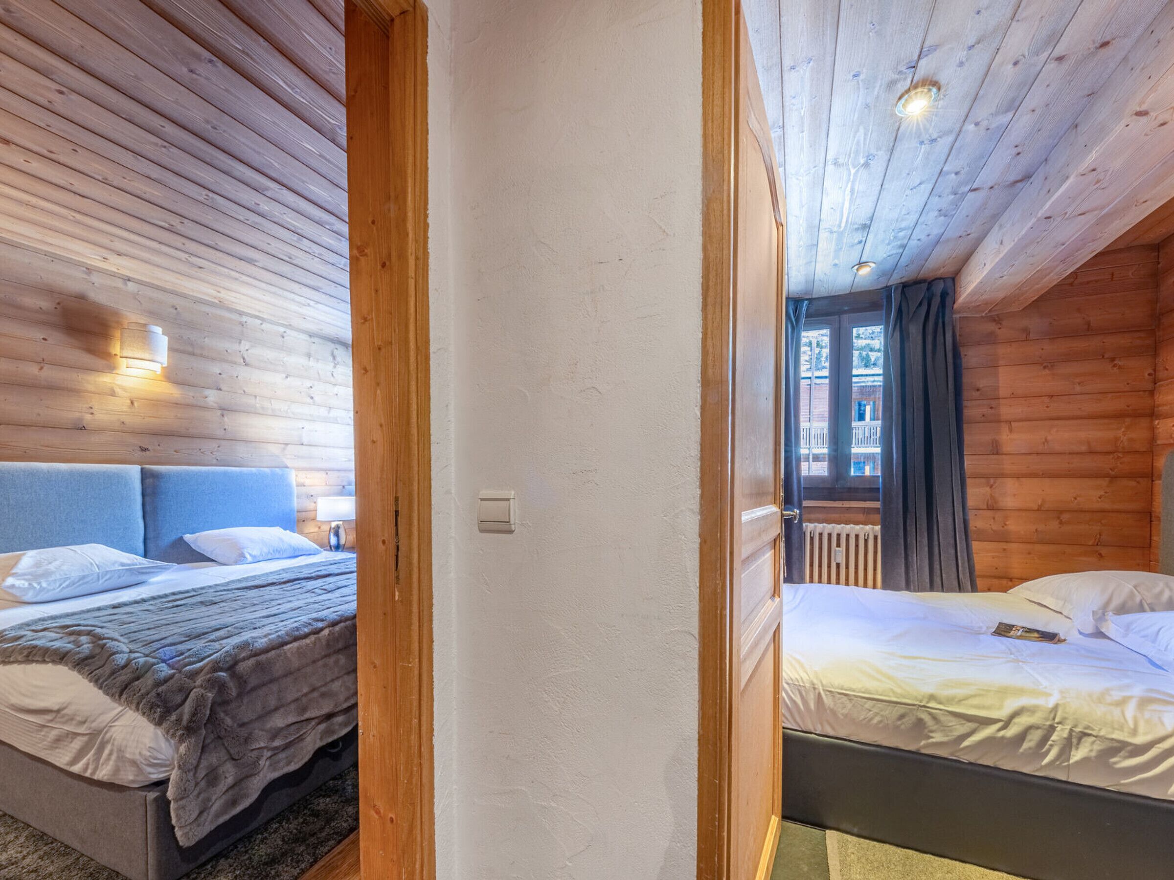 Een houten kamer met twee bedden, een raam met gordijnen en een lamp aan de muur.