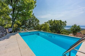 Piscina rectangular con agua azul cristalina, rodeada por un muro de piedra y barandillas de metal.