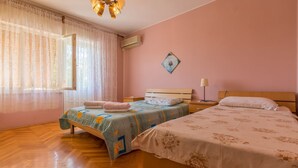 A bedroom with two beds, a window with sheer curtains, a wall-mounted air conditioner, and a small painting. - Dog-friendly apartment with private parking, BBQ area and large balcony (Grižane)
