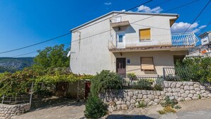 A two-story building with a balcony, a stone wall, and a view of the surrounding landscape. - Dog-friendly apartment with private parking, BBQ area and large balcony (Grižane)