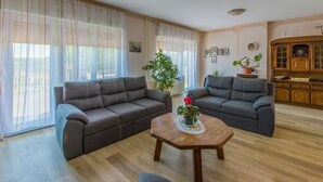 A living room with two grey sofas, a wooden coffee table with a potted plant, and a kitchen area with wooden cabinets. - Dog-friendly apartment with private parking, BBQ area and large balcony (Grižane)