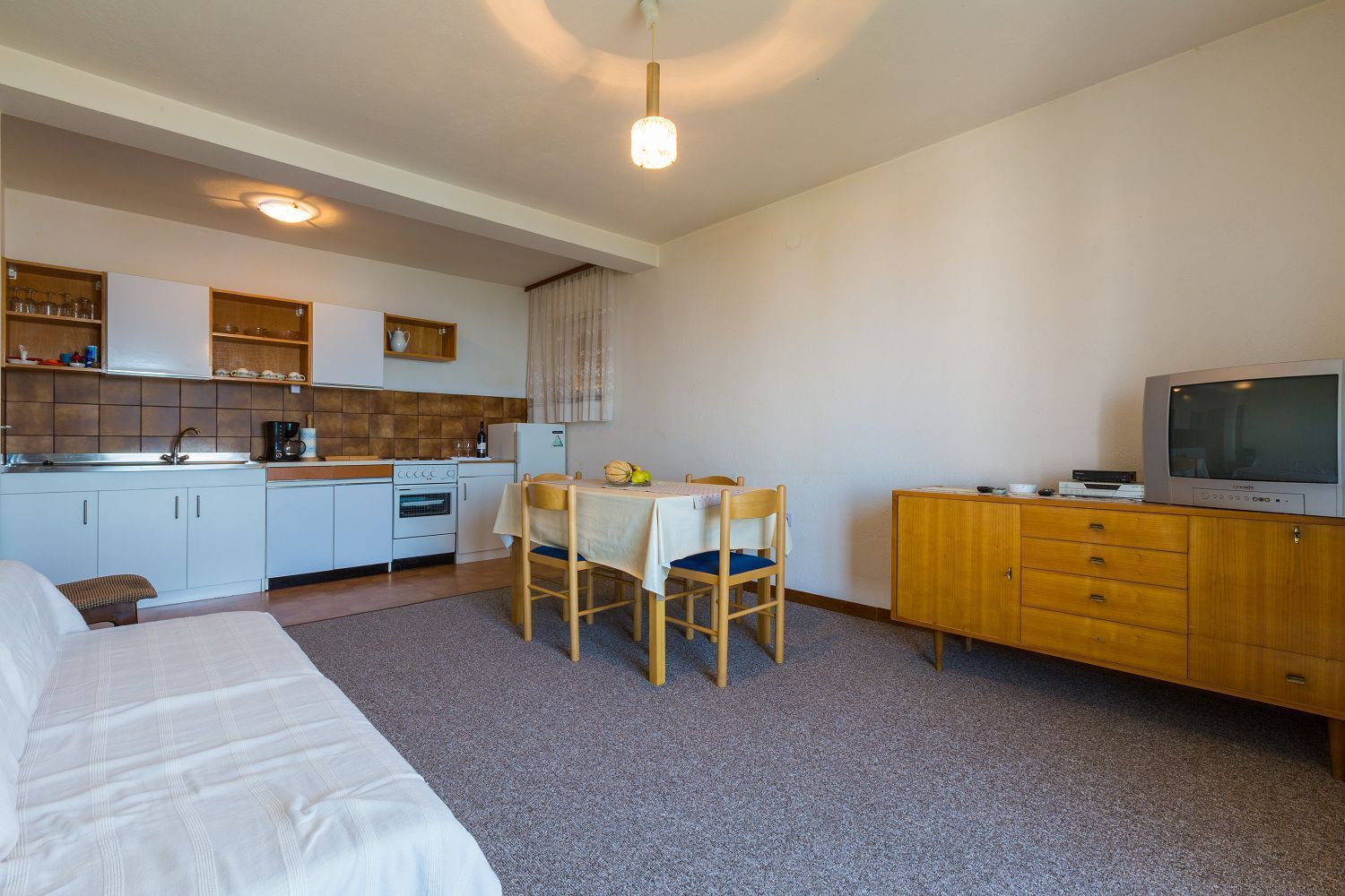 Ett kompakt hotellrum med ett litet kök, en matplats, en säng och en tv.