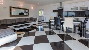 Una sala de estar moderna con piso a cuadros blanco y negro, un sofá gris, una zona de comedor con mesa de vidrio y una cocina con gabinetes blancos.