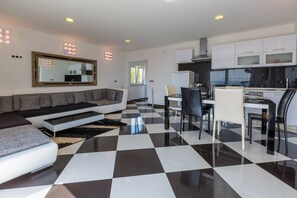 Ein modernes Wohnzimmer mit einem schwarz-weiß karierten Boden, einem grauen Sofa, einem Essbereich mit einem Glastisch und einer Küche mit weißen Schränken.