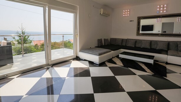 Una sala de estar moderna con suelo de cuadros, un sofá grande, un televisor y un balcón con vistas.