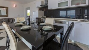 Una cocina moderna con armarios blancos, encimera negra y comedor con mesa negra y sillas blancas.