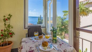Un balcón con una mesa dispuesta para el desayuno, una planta en maceta y vista al mar.