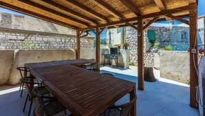 Eine Terrasse im Freien mit Holztisch und -stühlen, einem Grill und einer Steinwand im Hintergrund.