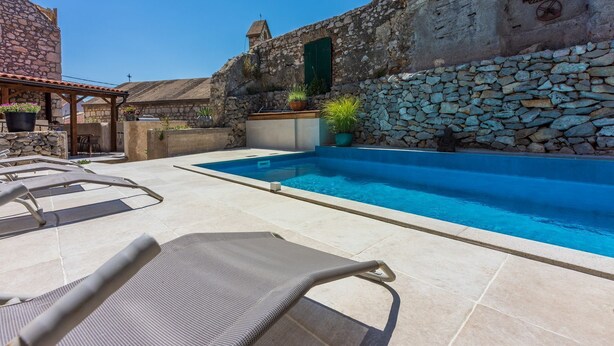 Ein Swimmingpool mit Liegestühlen, Steinmauern und einem rustikalen Gebäude mit einem Steindach.