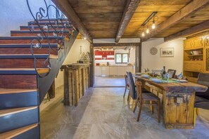 Un intérieur rustique avec un escalier en bois, un coin repas doté d’une table en bois et une cuisine à l’arrière-plan.