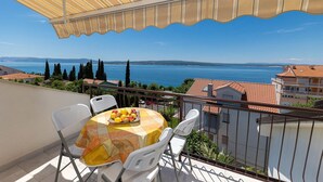 A balcony with a table set for two, overlooking a coastal view with buildings and trees. - Impressive apartment just 400 metres from the sandy beach with panoramic views (Crikvenica)