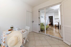 Ein Zimmer mit Esstisch für zwei Personen, einem grünen Sofa und einer Glasschiebetür, die in einen Küchenbereich führt.