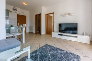 A modern living room with a flat-screen TV, a sofa, a coffee table, and a dining area with chairs. - Cosy apartment just 250 metres from the beach with sea view, private parking, WiFi (Dramalj)