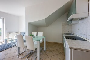 A modern kitchen with a dining area, featuring a glass table and white chairs, a built-in stove, and a view of the outdoors. - Cosy apartment just 250 metres from the beach with sea view, private parking, WiFi (Dramalj)