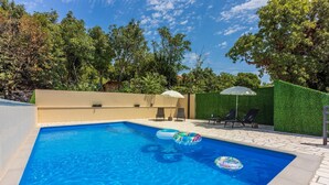 A rectangular swimming pool with clear blue water, surrounded by a tiled deck. There are lounge chairs and umbrellas, and a green hedge in the background. - Unique villa with private pool, sea view, trampoline, bikes and many hiking trails in the area (Jadranovo)