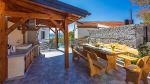 A covered outdoor dining area with wooden furniture and a stone wall. - Unique villa with private pool, sea view, trampoline, bikes and many hiking trails in the area (Jadranovo)